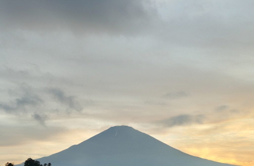 画像下部に富士山のシルエットが見え、画像上部は夕陽に照らされた曇り空が見える。